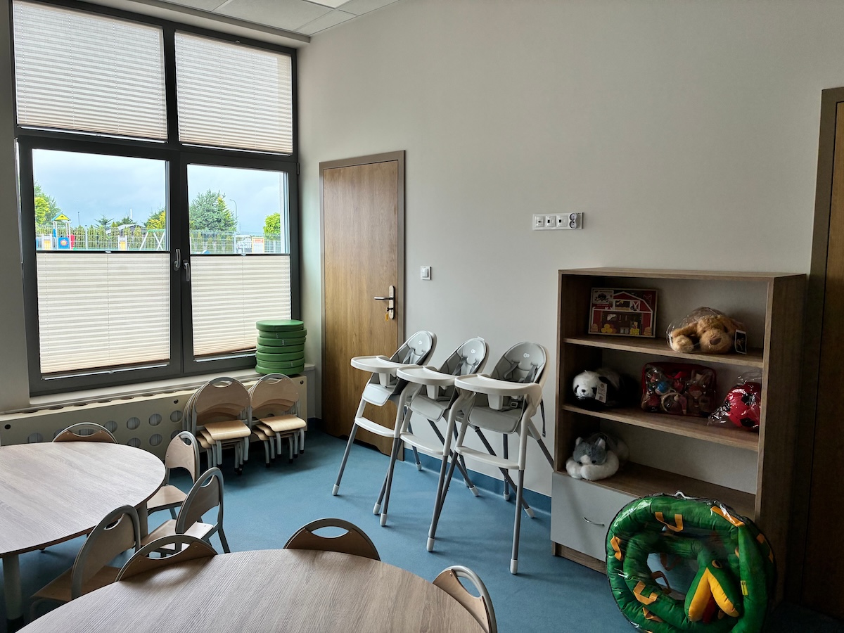 Sala ze stolikami, krzesełkami do karmienia i regałem z zabawkami